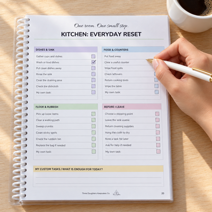 Hand checking off the kitchen everyday reset checklist in the printed ADHD cleaning planner, with a cup of coffee